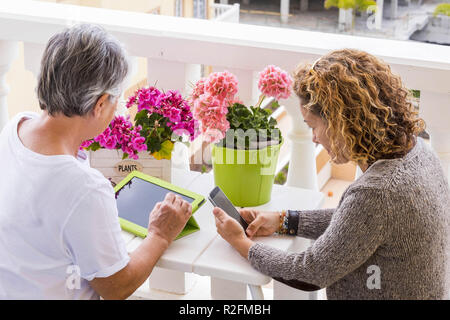 two adults woman different ages like mother and doughter use mobile technology tablet and smartphone outdoor in the terrace. happy search on internet for modern lifestyle Stock Photo