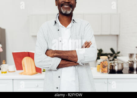 cropped view of african american man with arms crossed standing at kitchen Stock Photo