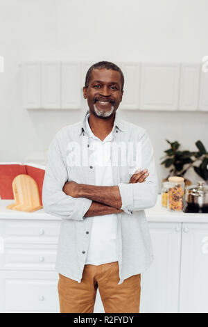 happy african american mature man with arms crossed standing at kitchen Stock Photo