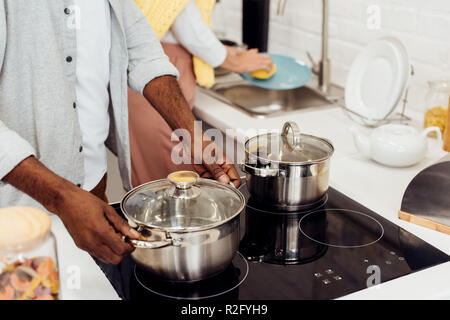 close up of african american man holding pot while woman washing dishes at kitchen Stock Photo