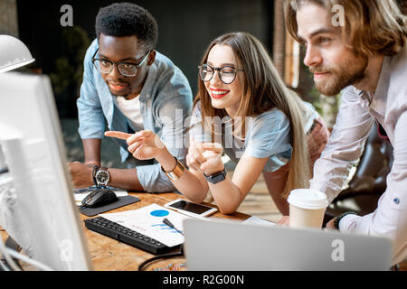 Group of young multi ethnicity coworkers dressed casually working together focused on the computer monitor indoors Stock Photo