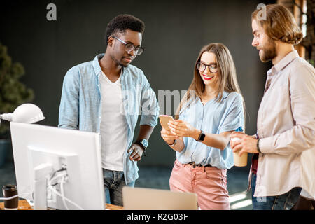 Group of a young multi ethnicity coworkers dressed casually talking together having fun at the modern office interior Stock Photo