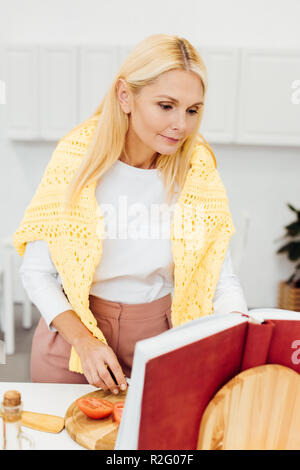 beautiful mature woman cooking and reading recipe in cookbook at kitchen Stock Photo