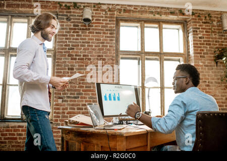 Two male coworkers working with analitycs in the beautiful office with brick wall on the background Stock Photo