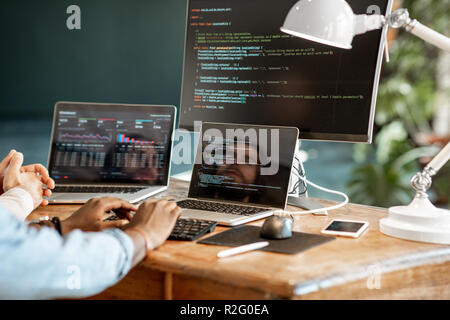 Programmers writing a program code sitting at the workplace with three monitors in the office. Cropped imaage with no face Stock Photo