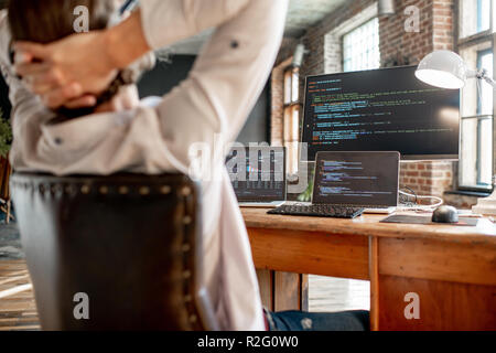 Young male programmer relaxing during the work with program code sitting at the workplace with three monitors in the office. Image focused on the screen Stock Photo