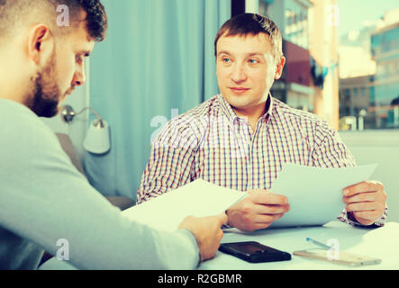 Portrait of two men in serious discussion at home table while analysing documents together Stock Photo