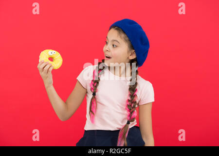 Kids huge fans of baked donuts. Impossible to resist fresh made donut. Girl hold glazed cute donut in hand red background. Kid smiling girl ready to eat donut. Sweets shop and bakery concept. Stock Photo
