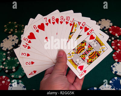 A person playing poker with a deck of poker cards in his hand and poker chips of various colors on a green mat Stock Photo