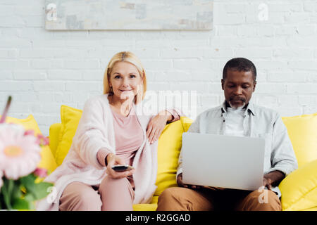 mature african american man using laptop while woman sitting on sofa with remote controller Stock Photo