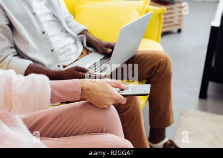 close up of african american man using laptop while woman pushing buttons on remote controller Stock Photo