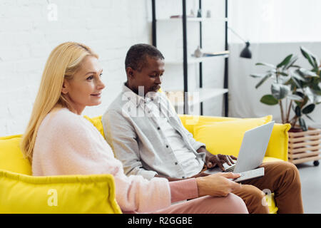 mature african american man using laptop while woman sitting on sofa with remote controller Stock Photo