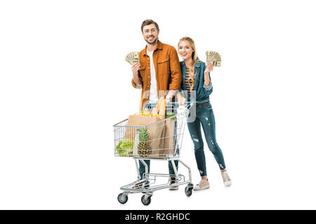 young happy couple showing cash money and carrying shopping trolley with food in paper bags isolated on white Stock Photo