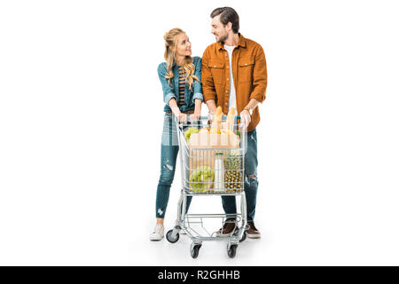 happy couple carrying shopping trolley with products and looking at each other isolated on white Stock Photo