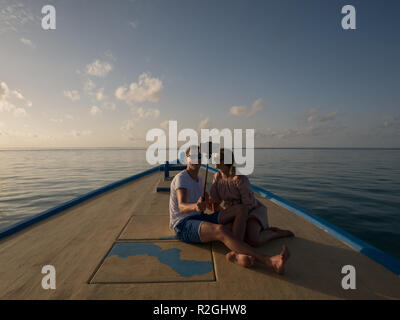 A couple on the bow of a boat sailing into the sunset in the Maldives, taking a selfie Stock Photo