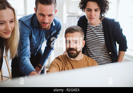 Group of young businesspeople looking at laptop screen in office, discussing issues. Stock Photo