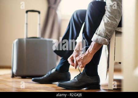 Midsection of businessman on a business trip sitting in a hotel room, tying shoelaces. Stock Photo