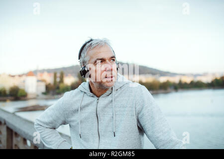 Mature male runner with headphones outdoors in city, listening to music. Stock Photo