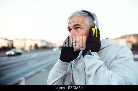 Mature male runner putting on headphones outdoors in city. Stock Photo
