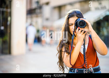 Beautiful teenager with long dark hair focused on taking photography in urban scenic Stock Photo