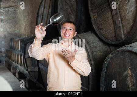 Happy customer holding glass of wine from wooden barrels in storage Stock Photo