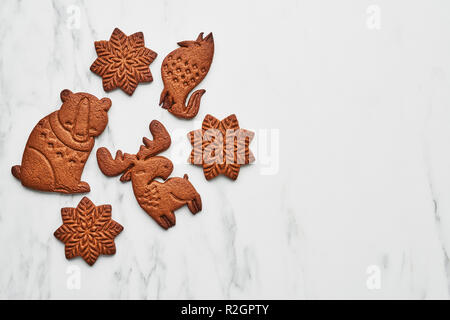Top view of snowflake, bear, elk and fox shape gingerbread cookies on white marble table with copy space. Stock Photo