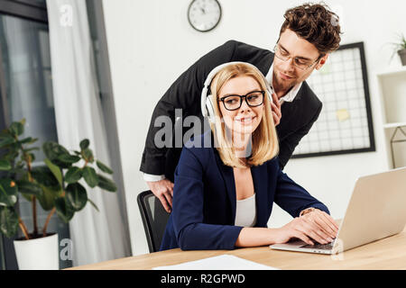 portrait of businessman flirting with colleague in headphones at workplace with laptop in office Stock Photo