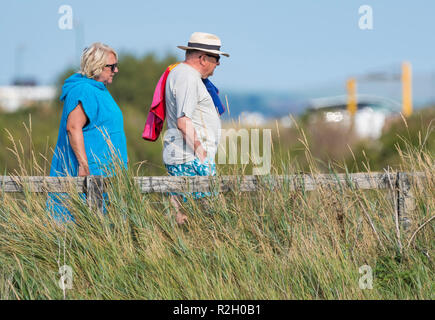 Side View of a middle aged man and woman walking carrying a towel in Summer in the UK. Stock Photo