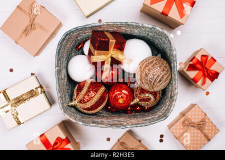 Silver box with presents and red balls surrounded by presents on white wooden background. Flat lay. Christmas concept. Stock Photo