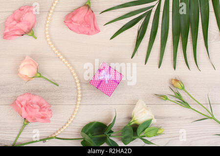Gift box, beads on a string with white and pink flowers, green leaves on wooden background. Woomen cosmetics. Top view. Stock Photo