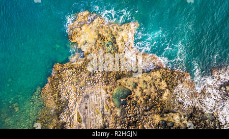 Aerial drone view of the ocean and waves crashing on rocks.A man alone swimming on a natural pool.