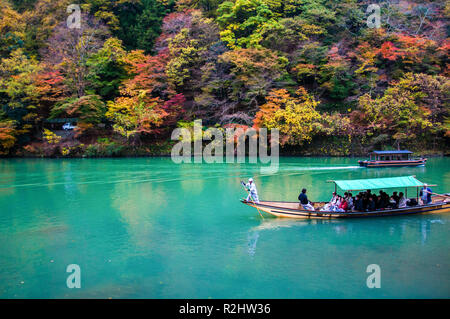 Kyoto, Japan - NOV 23, 2012: Traditional tourist boat pass on the emerald color Katsura river along the beautiful autumn leaves in Arashiyama Stock Photo