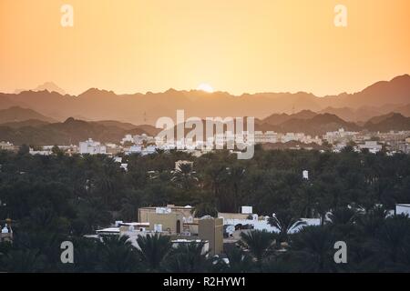 City against mountain range at idyllic sunset. Nizwa in Sultanate of Oman. Stock Photo