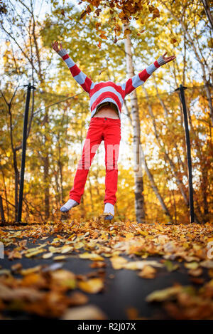 Boy jumping on a trampoline covered in autumn leaves, United States Stock Photo