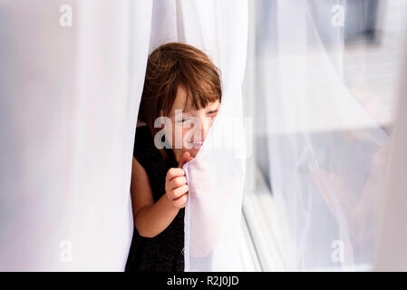 Smiling girl hiding behind a curtain Stock Photo