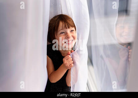 Girl hiding behind a curtain laughing Stock Photo