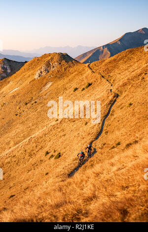 Man and woman mountain biking in the Austrian Alps at sunset near Gastein, Salzburg, Austria Stock Photo