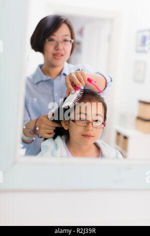 Mother brushing daughters hair in bathroom mirror Stock Photo