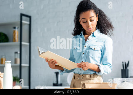 attractive african american girl holding cookbook in kitchen Stock Photo