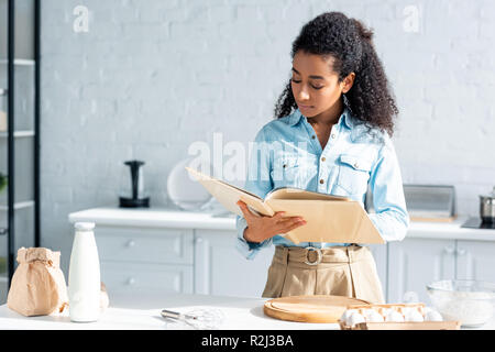 attractive african american woman reading cookbook in kitchen Stock Photo