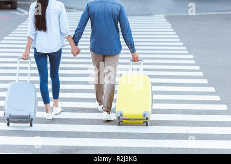 A couple of tourists crossing pedestrian, holding hands and pulling their luggage Stock Photo