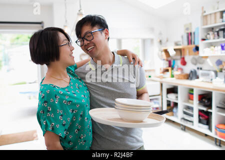 Affectionate couple hugging, doing dishes in kitchen Stock Photo