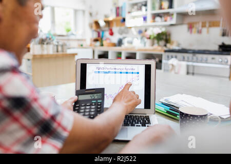 Senior man with calculator looking at investment chart on laptop Stock Photo