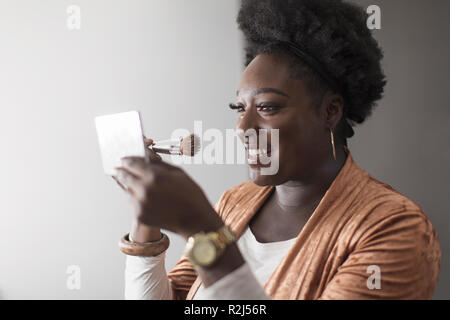 Smiling woman applying makeup in compact mirror Stock Photo