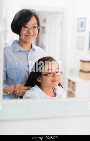 Mother fixing daughters hair in bathroom mirror Stock Photo