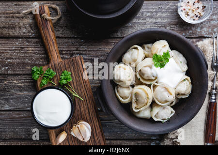 Traditional homemade Russian pelmeni meat dumplings with sour cream and greens over gray background. top view Stock Photo