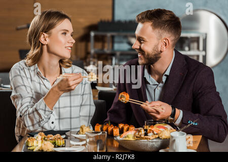 Lovely couple amorously looking at each other and eating sushi rolls in restaurant Stock Photo