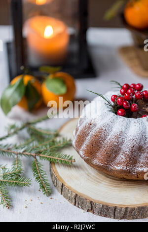 Christmas and new year's cake with berries and christmas tree brunch on craft paper at wood board, lantern behind and mandarins at white background Stock Photo