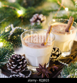 Christmas Traditional Homemade Eggnog in Festive Atmosphere. Fir branches with Christmas Lights and Decorations. Milk Cocktail with Spice. Selective F Stock Photo