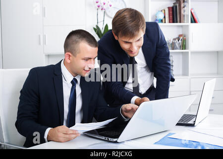Two young business men colleagues working together with laptops on desk in office Stock Photo